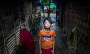 म्याँमार में विस्थापितों के लिये बनाए गए एक शिविर में, अपने घर के बाहर खड़ी एक लड़की.