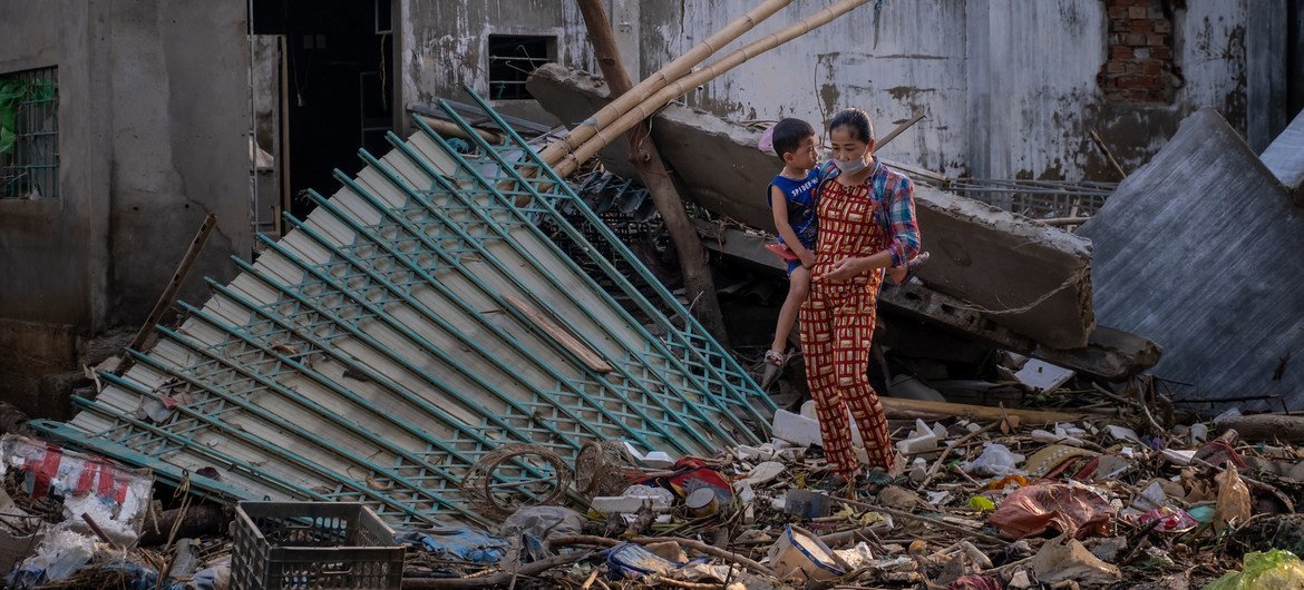 越南的一名妇女带着她的孩子走过最近被洪水摧毁的一栋房屋的废墟。