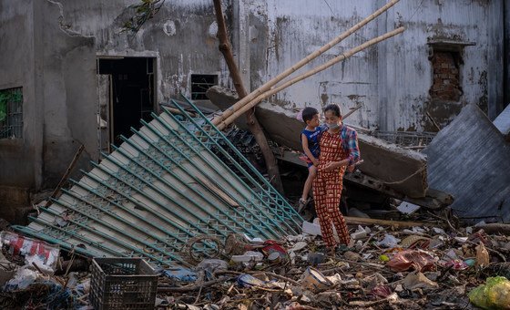 A woman carries her child as she walks past the ruins of a house destroyed by recent floods central Viet Nam. (October 2020)