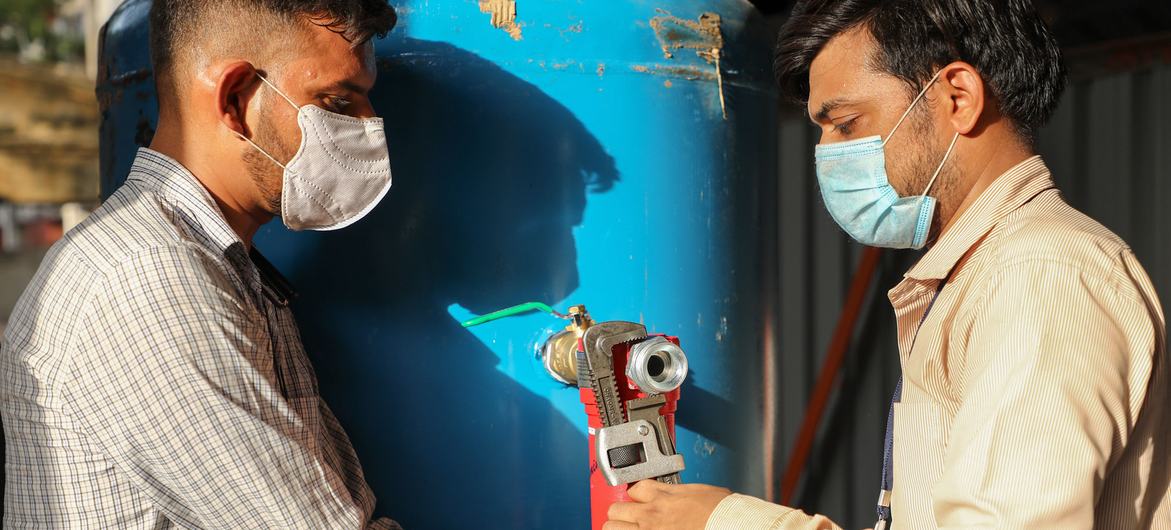 Two workers set up the oxygen cylinders for treating patients with respiratory diseases, in India.