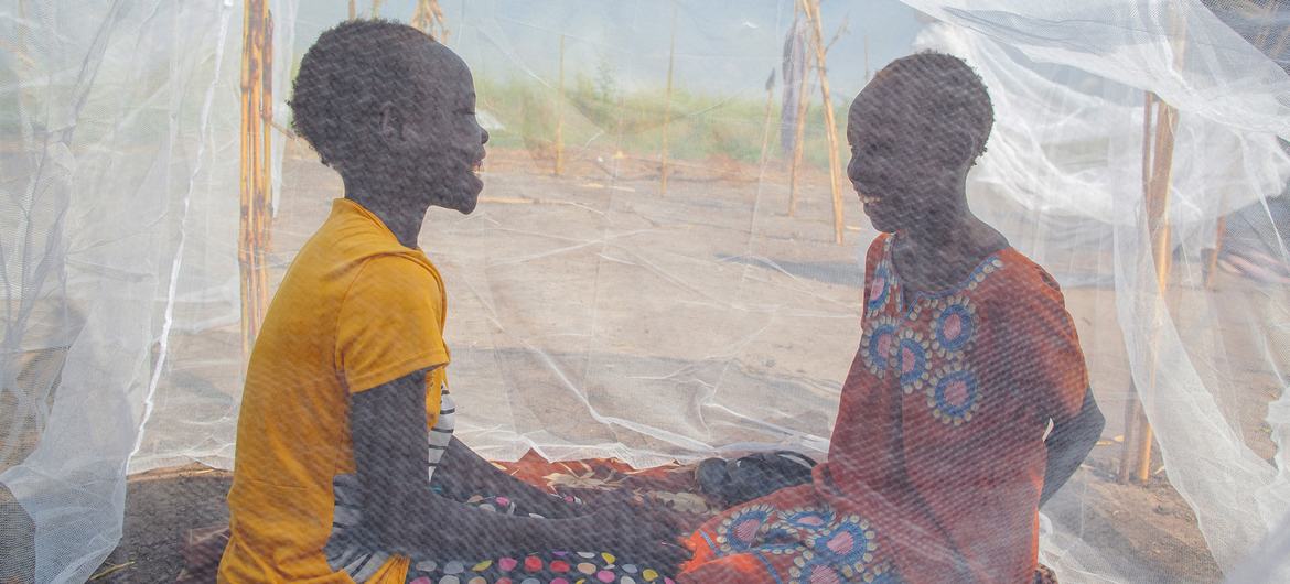 दक्षिण सूडान के बियेनिथियांग में, दो बच्चियाँ एक मच्छरदानी में बैठकर बात कर रही हैं. 