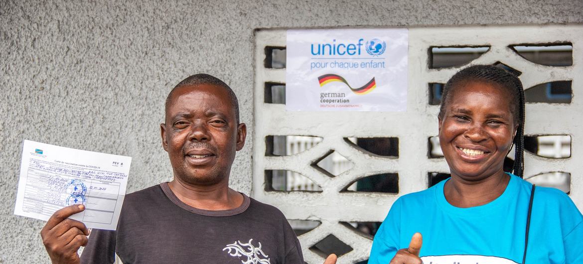 联合国儿童基金会支持的社区外展工作者布丽吉特和刚果民主共和国金沙萨的一位居民恩塞勒（N'Sele）。恩塞勒手持他的新冠疫苗接种卡。