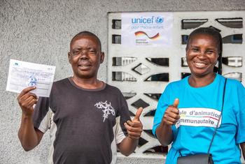联合国儿童基金会支持的社区外展工作者布丽吉特和刚果民主共和国金沙萨的一位居民恩塞勒（N'Sele）。恩塞勒手持他的新冠疫苗接种卡。