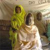 مجموعة من النساء المشردات داخليا يجلسن أمام لافتة للاحتفال باليوم العالمي للمرأة، في مخيم للنازحين في غرب دارفور، السودان. من صور الأمم المتحدة