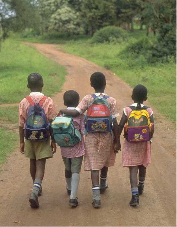 Quatre enfants en uniforme scolaire descendent un chemin de terre avec des sacs à dos, deux d'entre eux marchant bras dans le bras.