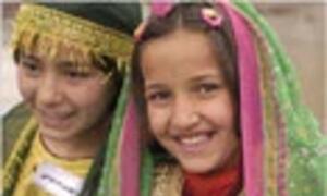 Two smiling young girls wearing colorful, embroidered traditional clothing and headscarves.