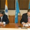 Two men sign a document at a table during a formal ceremony, with the flags of India, the World Bank, and IFAD in the background.
