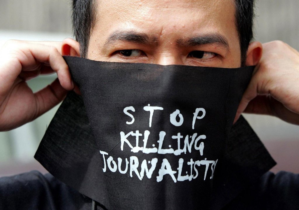 Un homme portant un masque où est inscrit le message : « arrêter de tuer les journalistes ».