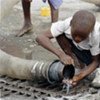 A young boy getting a drink of water from an open pipe.