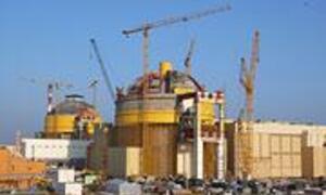 Construction site of a nuclear power plant with a large reactor building and multiple cranes.