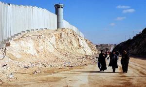 Palestinian women walk by Israel's barrier near Ramallah in the West Bank.
