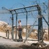 A settler security officer locking a gate in a fence separating Palestinians from their land