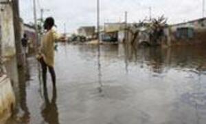 A person wades through a flooded street in a rural community, with houses and buildings in the background.