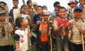 A group of smiling children and boys, some wearing hats, stand together outdoors in a rural setting.