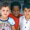 Three children in Akko draw together and smile for the photographer's camera.