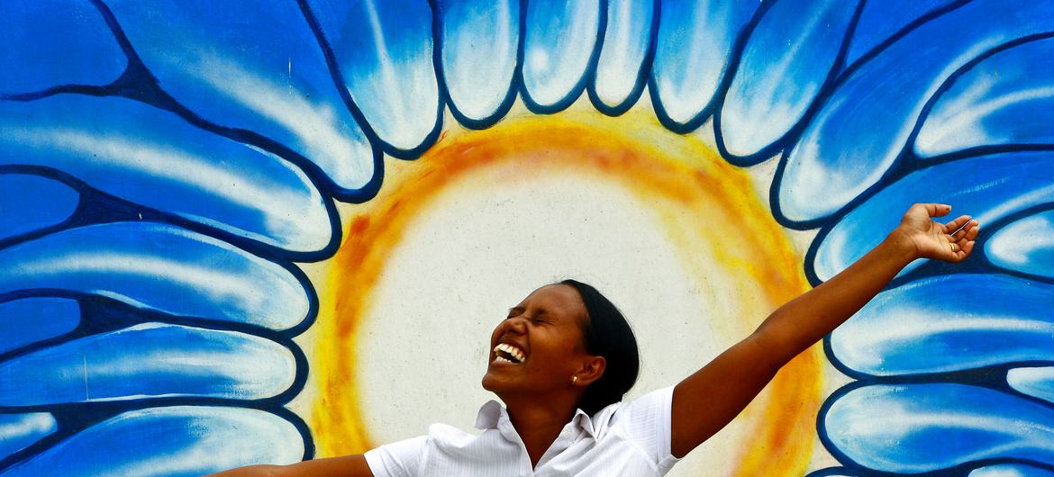 Une femme pose devant un dessin représentant le soleil à l'occasion de la célébration de la Journée mondiale de la santé mentale. Photo ONU/M. Perret
