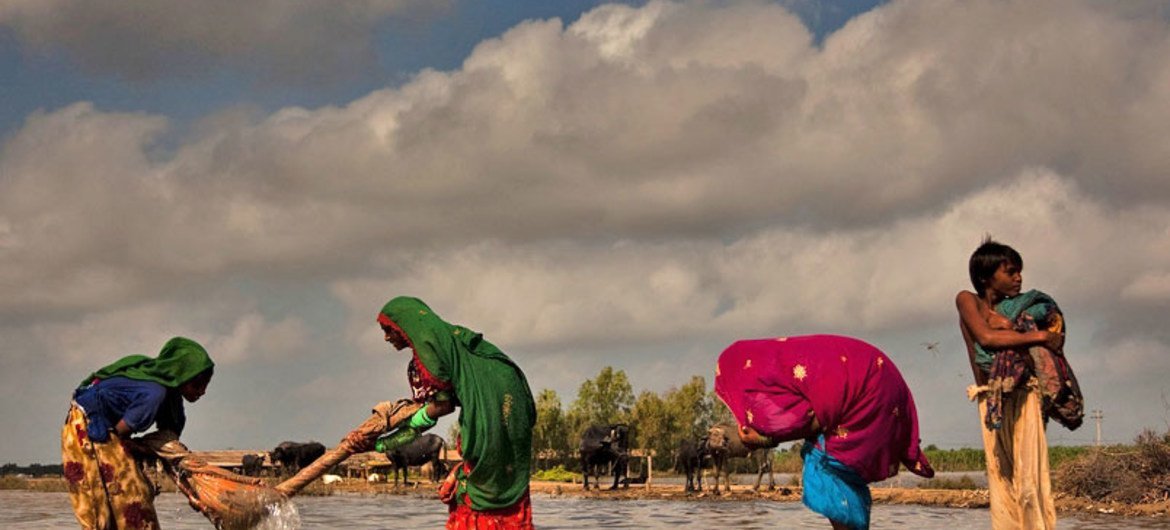 A flood-affected family in Pakistan washing clothes in rising floodwaters next to their temporary camp in Digri, Sindh province
