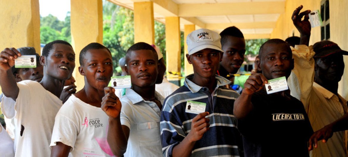 Youths display their voters ID cards as they wait in line to vote in Freetown.