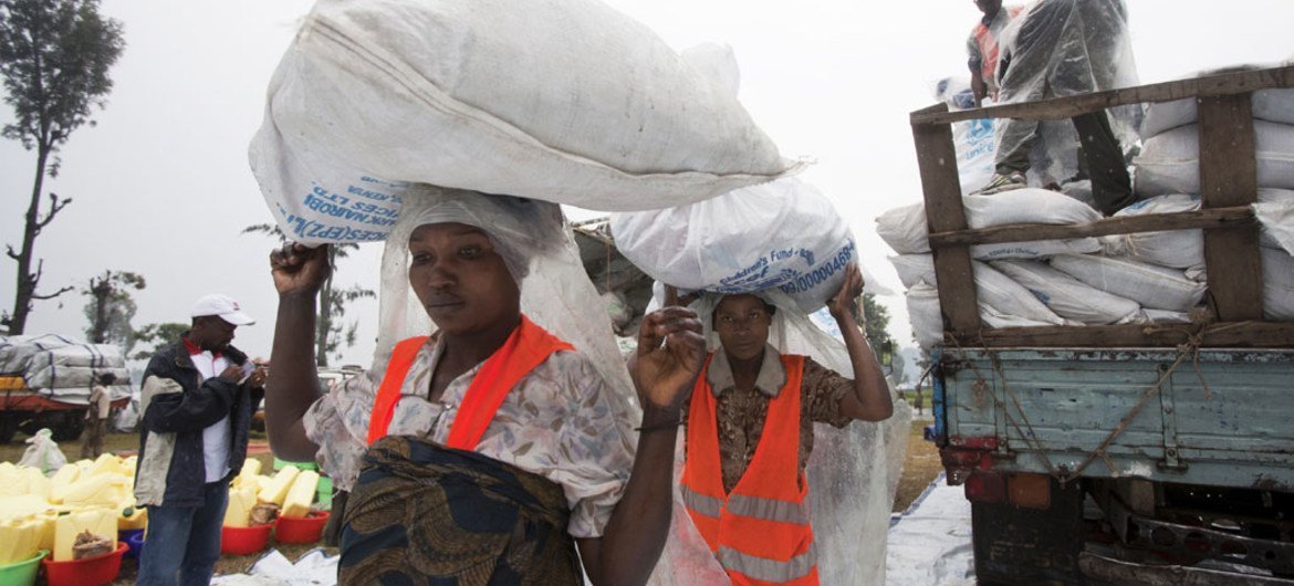 Dans le camp de personnes déplacées de Kanyaruchinya, à Goma, des femmes portent de larges sacs de riz distribués par l'UNICEF.
