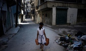Une fillette porte des jerricans d'eau, le long de débris dans une rue d'Alep, en Syrie. UNICEF/NYHQ2012-1293/Romenzi