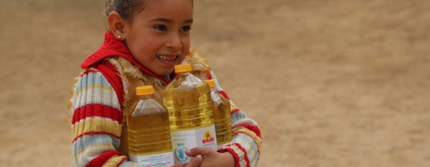 Une petite syrienne porte des bouteilles d'huile fournies par le PAM. Photo: PAM/Abeer Etefa