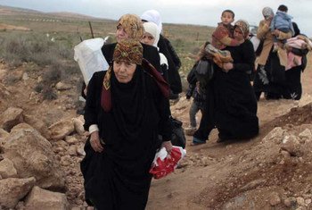 A line of Syrian refugee women, some carrying children, cross into Jordan from southern Syria.