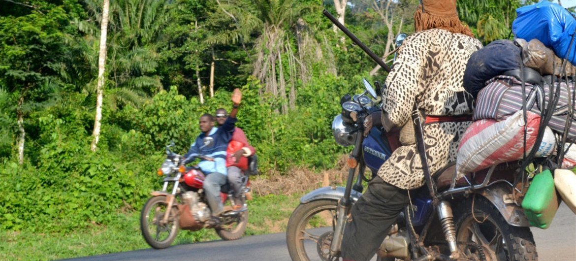 Passers-by on a motorcycle wave to ‘dozos’ posted along the road between Man and Duékoué in western Côte d’Ivoire.
