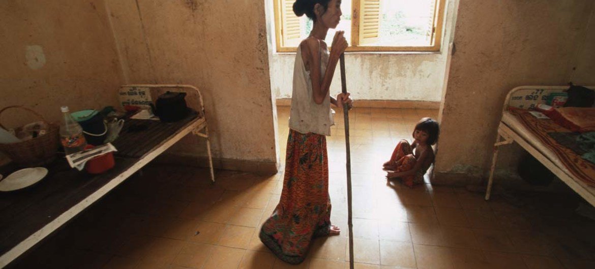 A woman suffering from HIV/AIDS in Cambodia uses a stick to walk back to her bed in hospital.