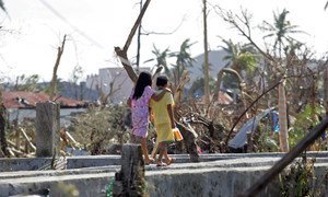 Two children walk past downed trees and other destruction caused by Super Typhoon Haiyan in Tacloban City.