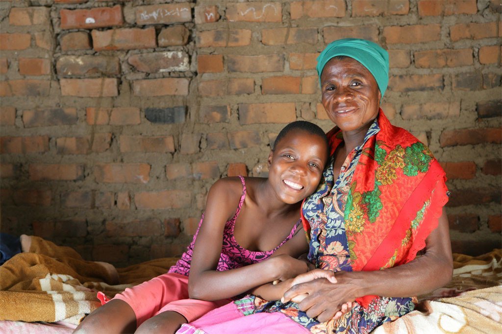 津巴布韦马库兹泽村的艾滋病病毒呈阳性的莫妮卡和她的孙女坐在家中的床上。