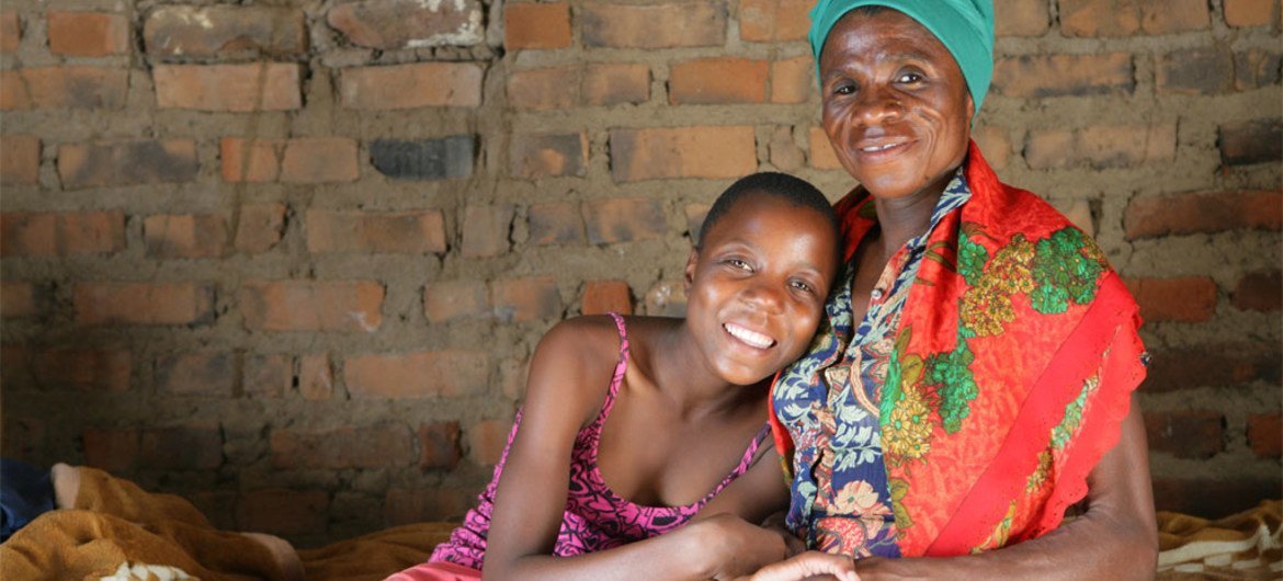 HIV positive Monica and her granddaughter sit at home on a bed in their village of Makuzeze, Zimbabwe.