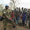 A peacekeeper stands guard at UN House while displaced children look on behind a fence.