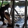 A woman in a conical hat feeds ducks from a basket at a pond.