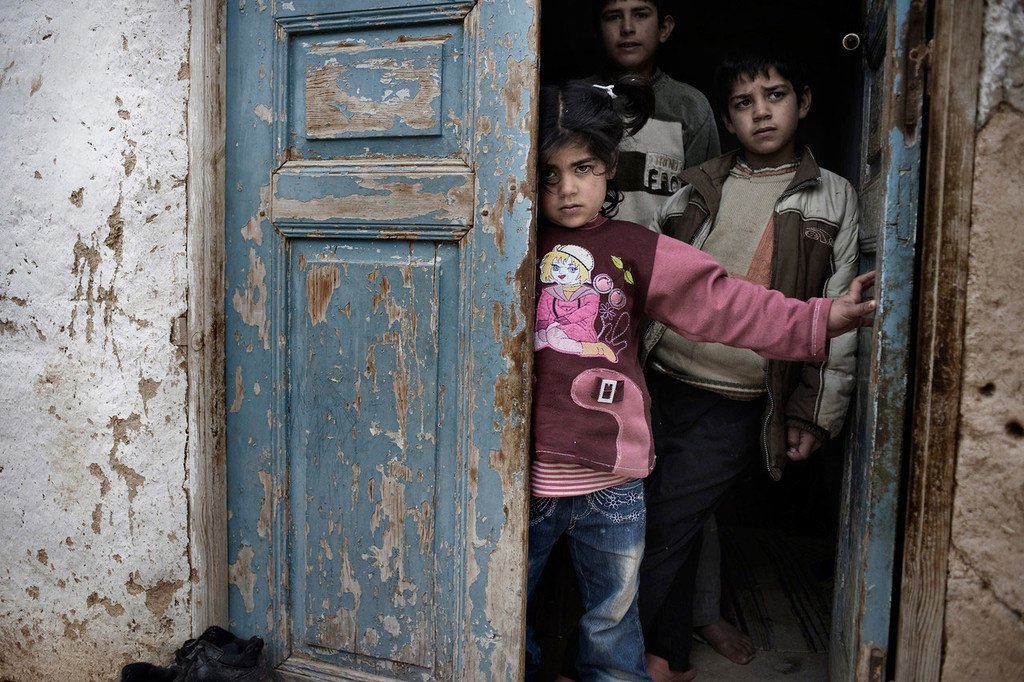 Des enfants syriens s'abritent derrière la porte d'une maison, au milieu de tirs et de bombardements, dans une ville touchée par le conflit.