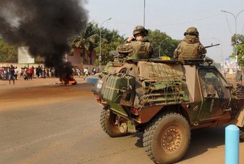 French troops patrol a street in Bangui, Central African Republic, as the body of a man lynched by a mob burns in the distance.