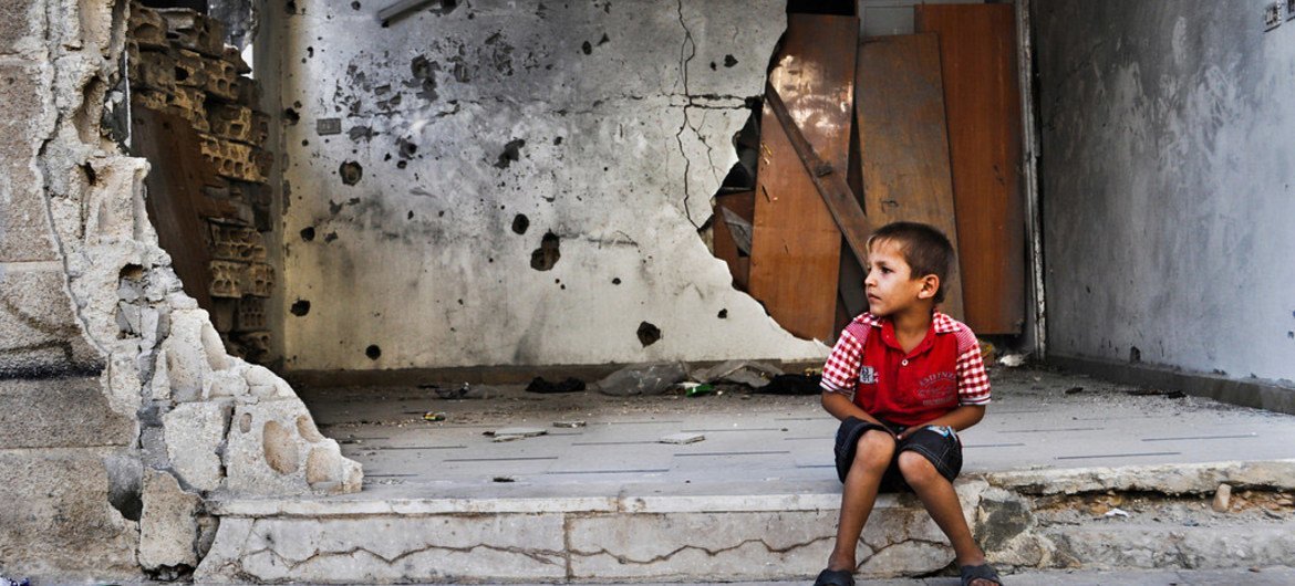 A young boy sits in front of a destroyed building in Homs, Syria.