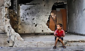 A young boy sits in front of a destroyed building in Homs, Syria.