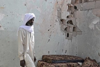 A resident of Tayuri stands against a bullet-riddled wall of his house, part of which was destroyed during clashes in Libya.