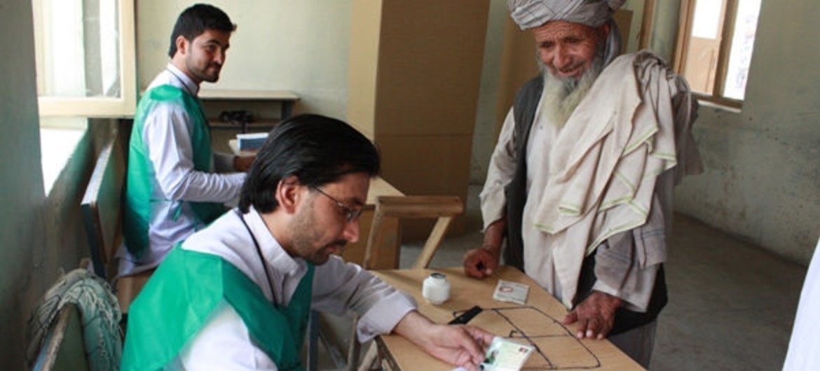 Electoral workers in Afghanistan (left) assisting a voter in the 14 June 2014 second round run-off in the country's presidential elections.