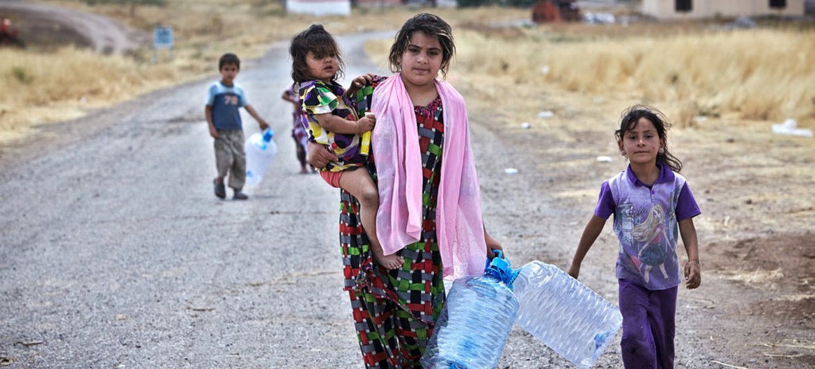 An Iraqi woman from Mosul holds her daughter in one hand and empty water containers in the other. Two other children follow her in search of water near the Garmava temporary camp in central Iraq.