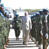 A man in a suit walks between two lines of soldiers in camouflage uniforms and blue berets during an inspection.