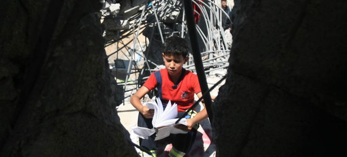 A boy looks through a schoolbook as he sits in the rubble of a home destroyed during an Israeli air strike on the city of Khan Yunis.