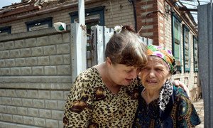 An elderly returnee to Sloviansk, Ukraine, whose house was hit by artillery and needs major repairs, is comforted by a relative.