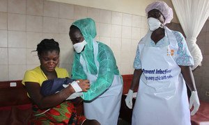 Two midwives in Ebola protective gear supplied by UNFPA hand over a newborn to her mother at the Star of the Sea Clinic in West Point, Monrovia, Liberia.