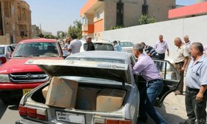 A family displaced from the Nineveh governorate in Iraq loads WFP food parcels into a car outside a distribution site in Erbil.