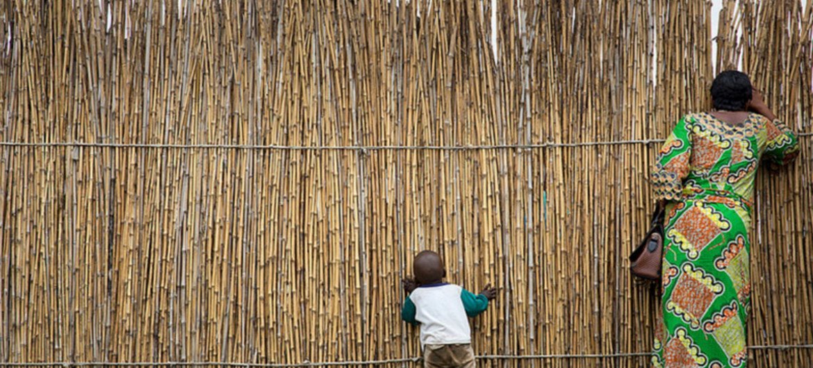 刚果民主共和国北基伍省，一位妇女和她的孩子隔着日托中心的竹篱笆向外张望。