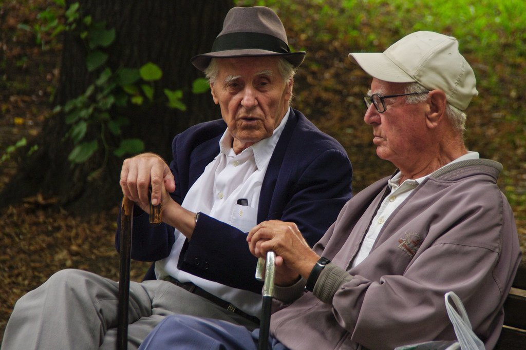 Dos hombres mayores conversan en el banco de un parque. 