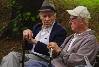 Two elderly retirees chat on park bench.