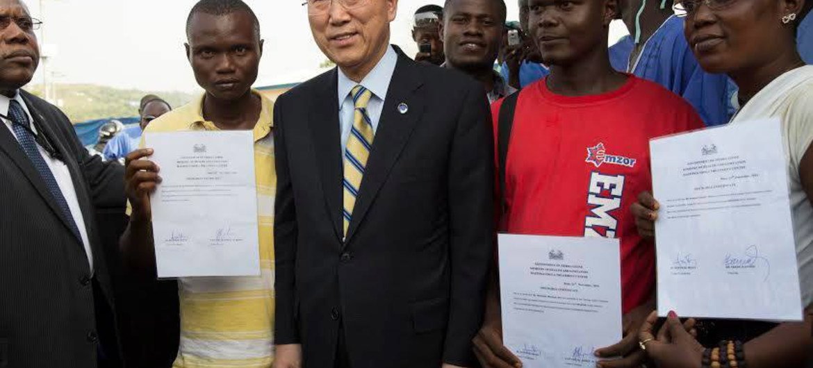 Secretary-General Ban Ki-moon (centre) stands with Ebola survivors in Sierra Leone, seen here showing their hospital discharge certificates.