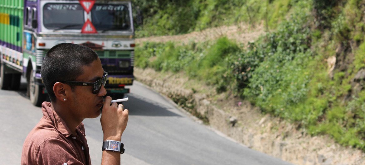 A man smokes on the side of the road as a bus passes in Nepal.